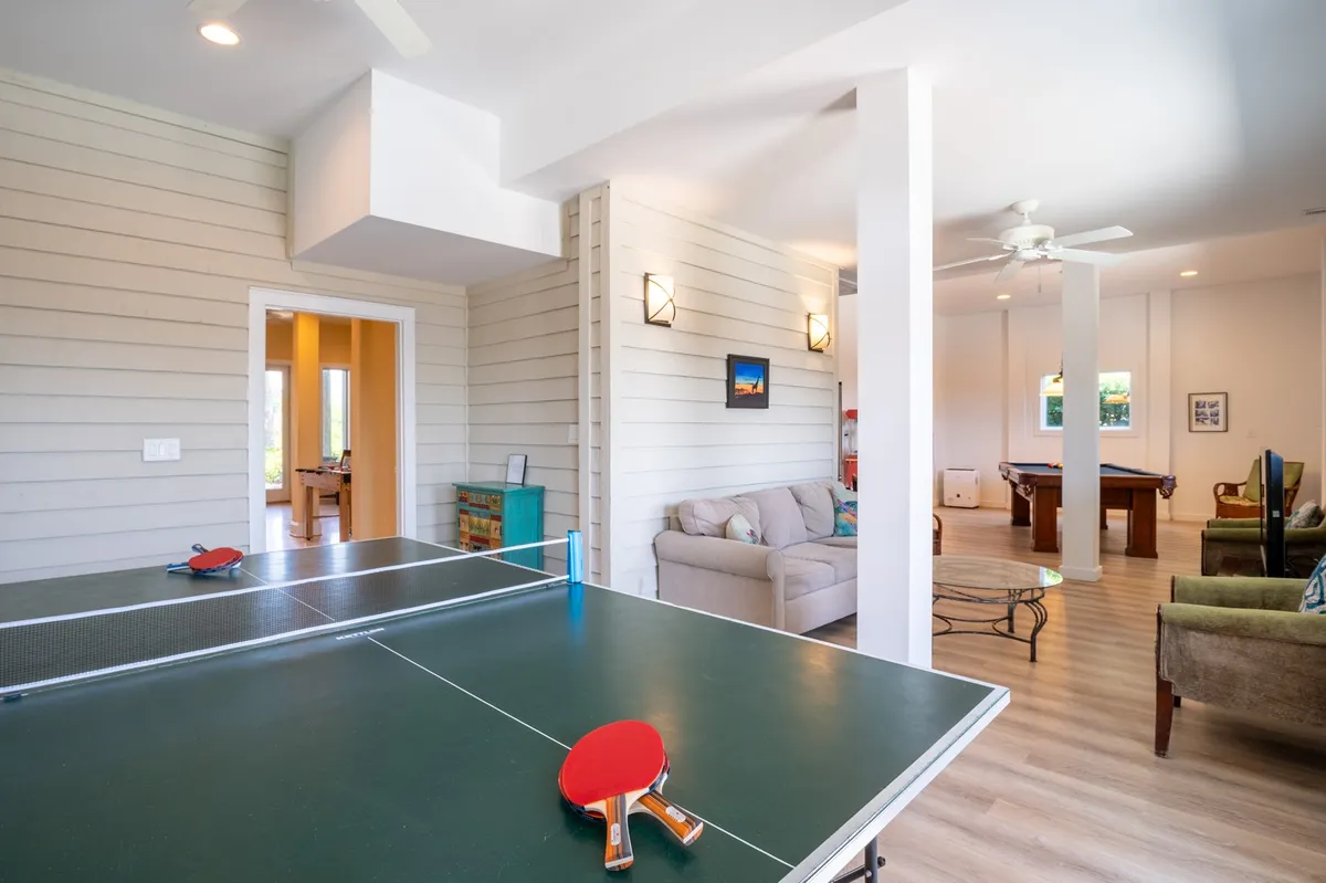 A spacious recreation room with a ping pong table, pool table, and a comfortable sofa under warm lighting. The area is set up for both competitive games and relaxed lounging, embodying the playful, multi-activity spirit described in the text.
