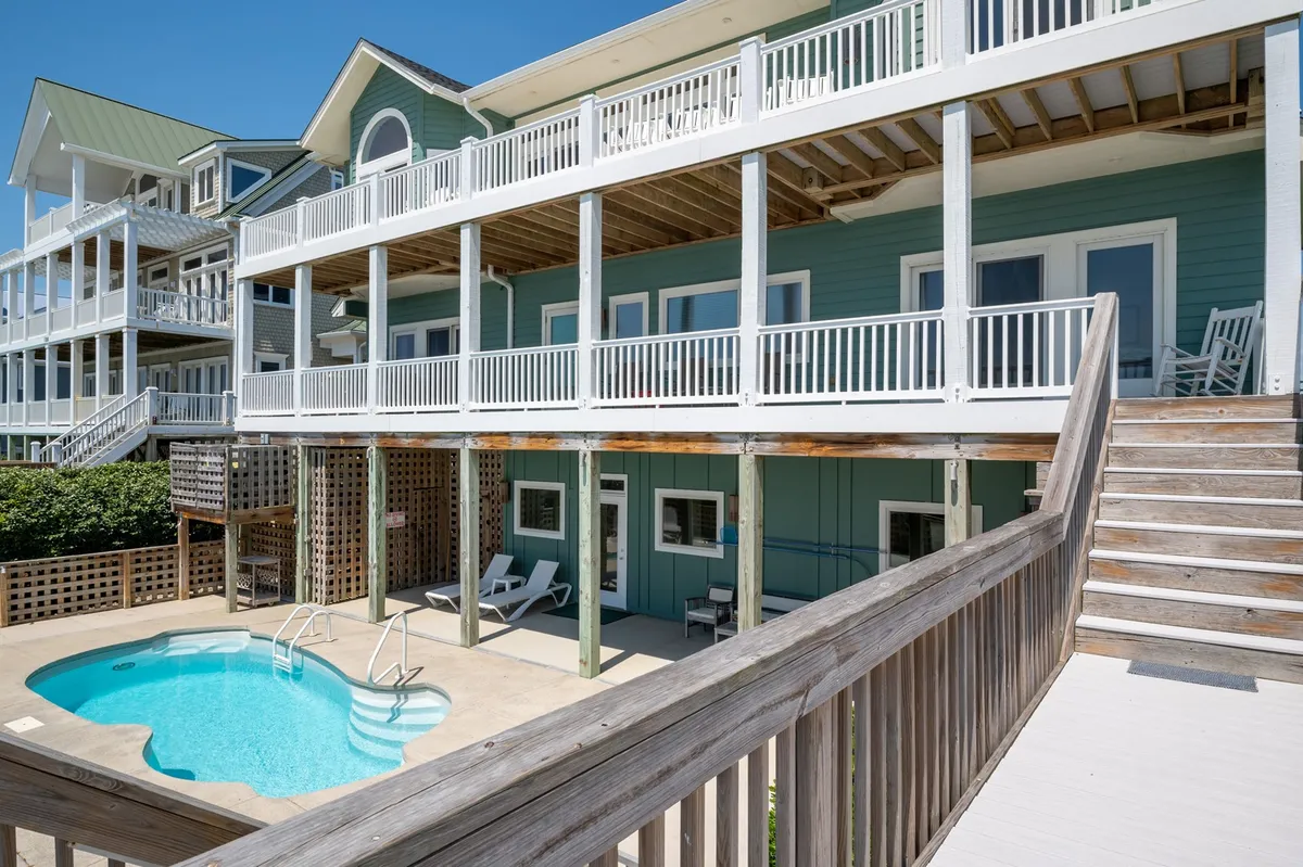 An exterior view featuring a sparkling swimming pool surrounded by a spacious deck and a balcony with outdoor seating. The inviting pool area is framed by the house and hints at sunset views, capturing opportunities for both relaxation and family fun back at the estate.