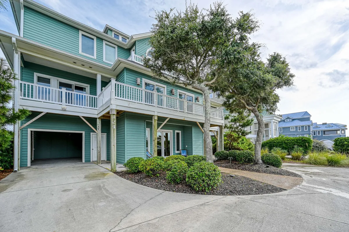 The exterior shot shows the home's blue façade, landscaped garden, multiple balconies, and a spacious, curving driveway that can accommodate several vehicles. The setting is inviting and signals both exclusivity and ample parking.