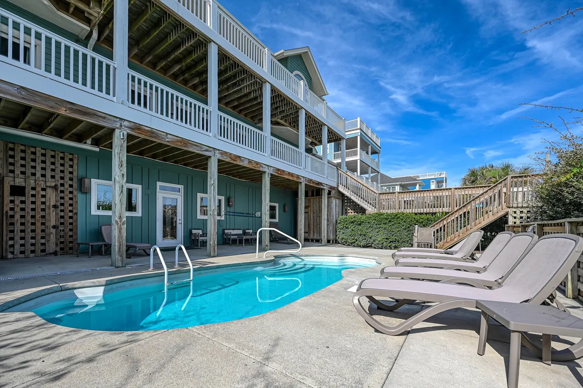 This exterior image captures the inviting swimming pool surrounded by reclining chairs and a spacious deck area. Stairs lead up to the main property, and the scene is bathed in natural light, suggesting a tranquil and leisurely atmosphere ideal for summer activities like swimming, sunbathing, and socializing outdoors.