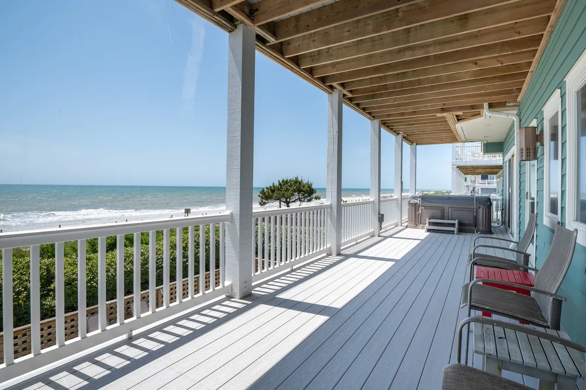 An exterior shot of a wooden deck with a hot tub overlooking the ocean. There is ample seating for guests, the sea stretches out in the background, and the setting feels calm and private—ideal for unwinding and enjoying ocean views across multiple seasons.
