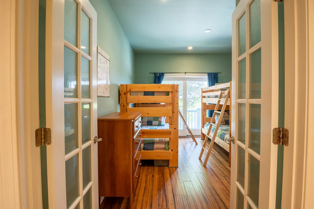 A cheerful and spacious bunk room with multiple bunk beds, a large window with curtains letting in daylight, and a wooden dresser. The room invites both play and relaxation, ideal for children and friends seeking comfort and fun memories.