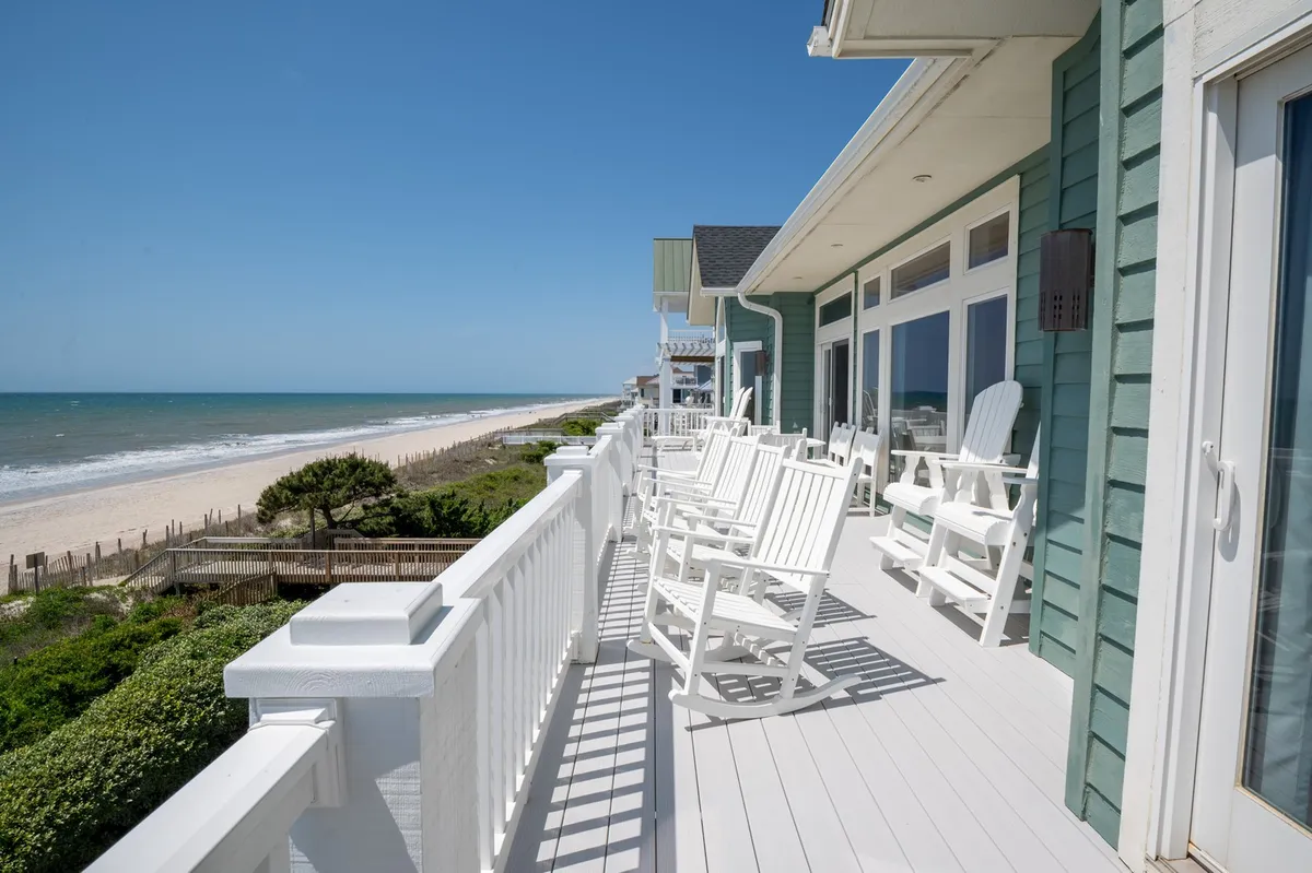 A covered deck with rocking chairs overlooking a breathtaking beach view and the vast ocean beyond. The deck invites guests to relax outdoors, listen to the waves, and savor gentle breezes, perfectly extending the bedroom sanctuary experience.