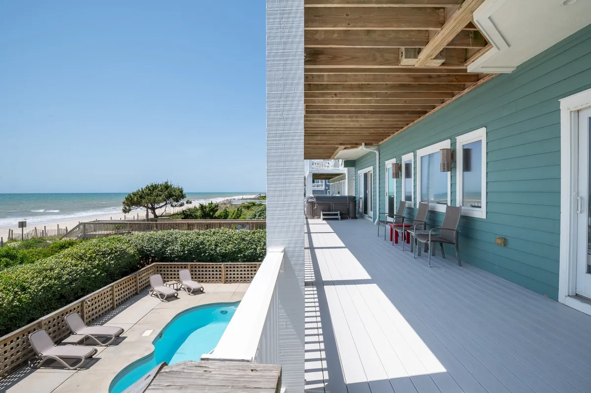 A serene deck area with a sparkling swimming pool, comfortable seating, and a clear ocean view beyond. The layout invites outdoor relaxation, sunbathing, and family or group activities, all with the ocean as a stunning backdrop.