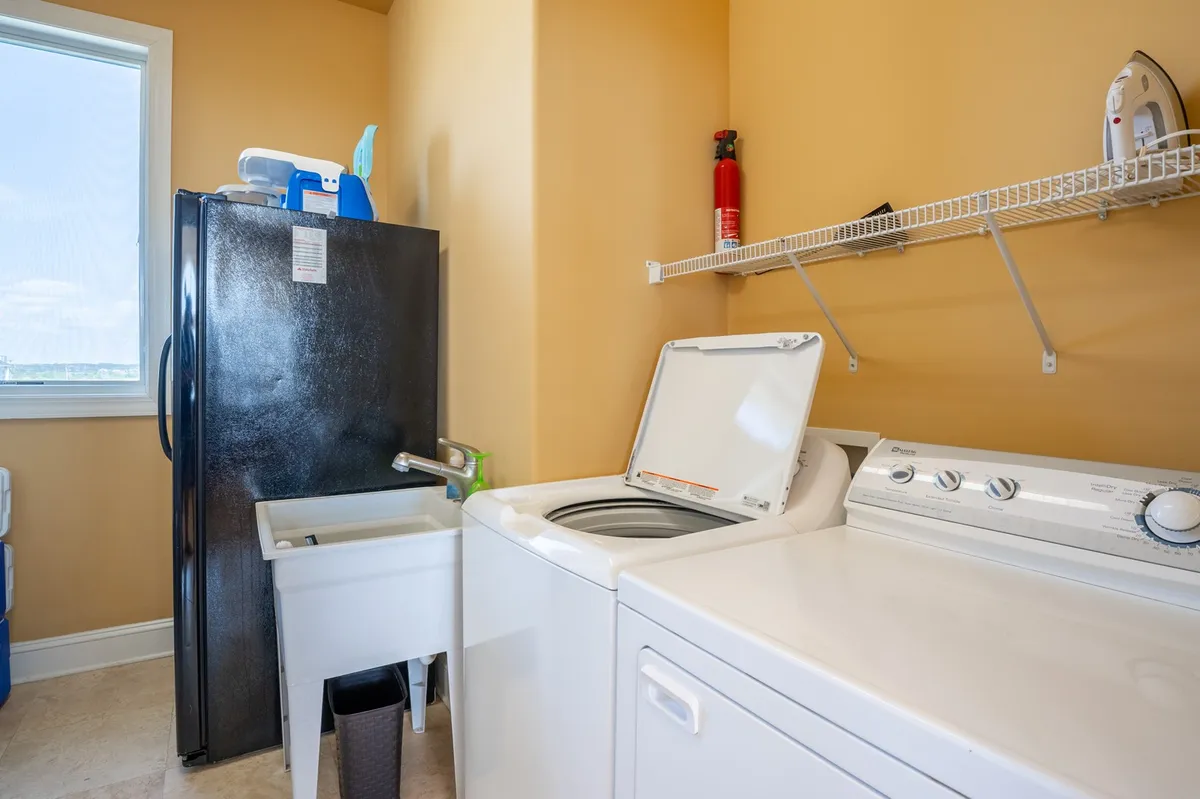 A dedicated laundry room with a washing machine, dryer, refrigerator, and utility sink. The room is bright and functional, representing the practical, family-friendly amenities designed to make large group stays more comfortable.