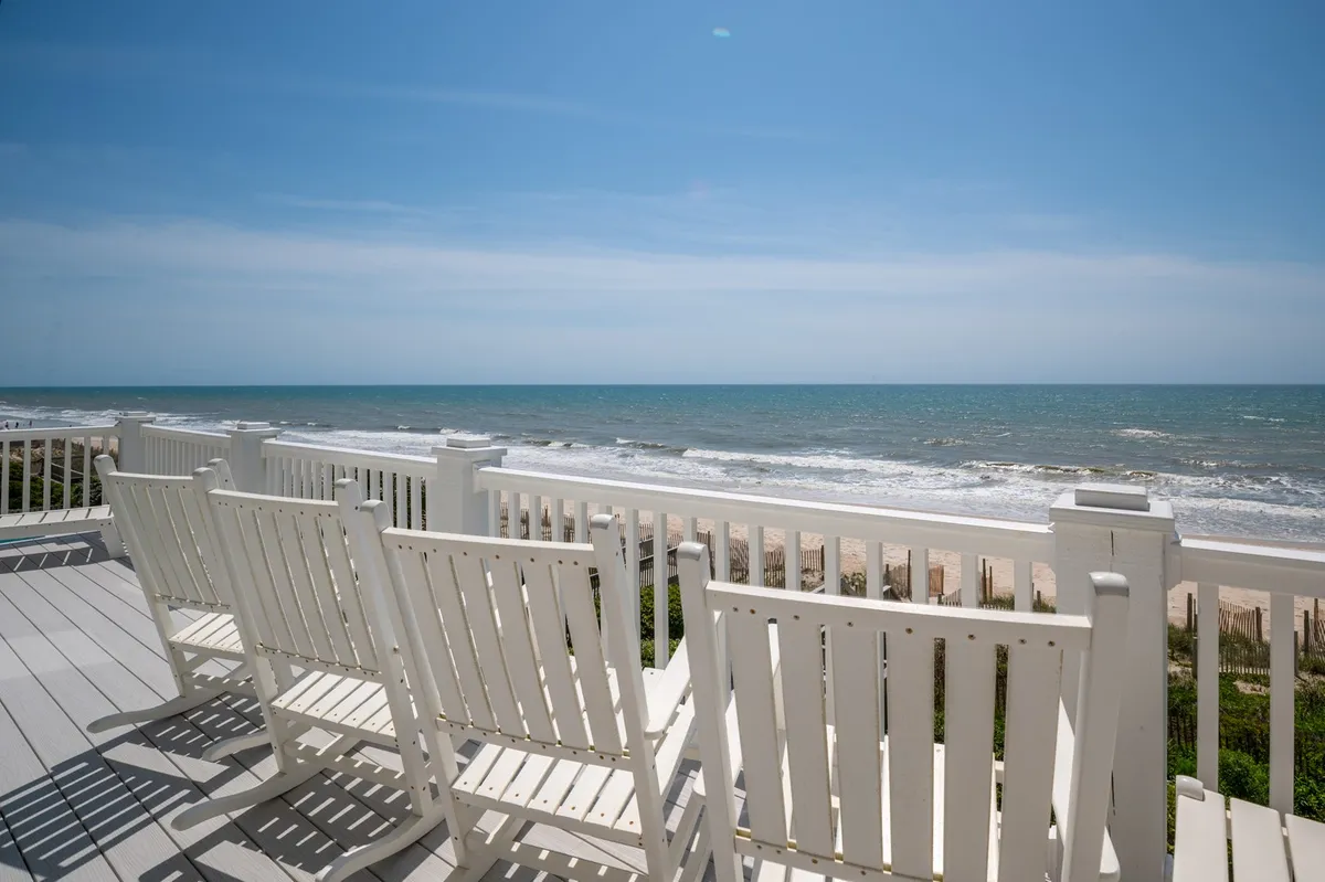 A serene view scene with white chairs set up to face the endless blue ocean under a clear sky. The image evokes peaceful moments of relaxation and the simple pleasure of watching the sunrise or sunset over the water.
