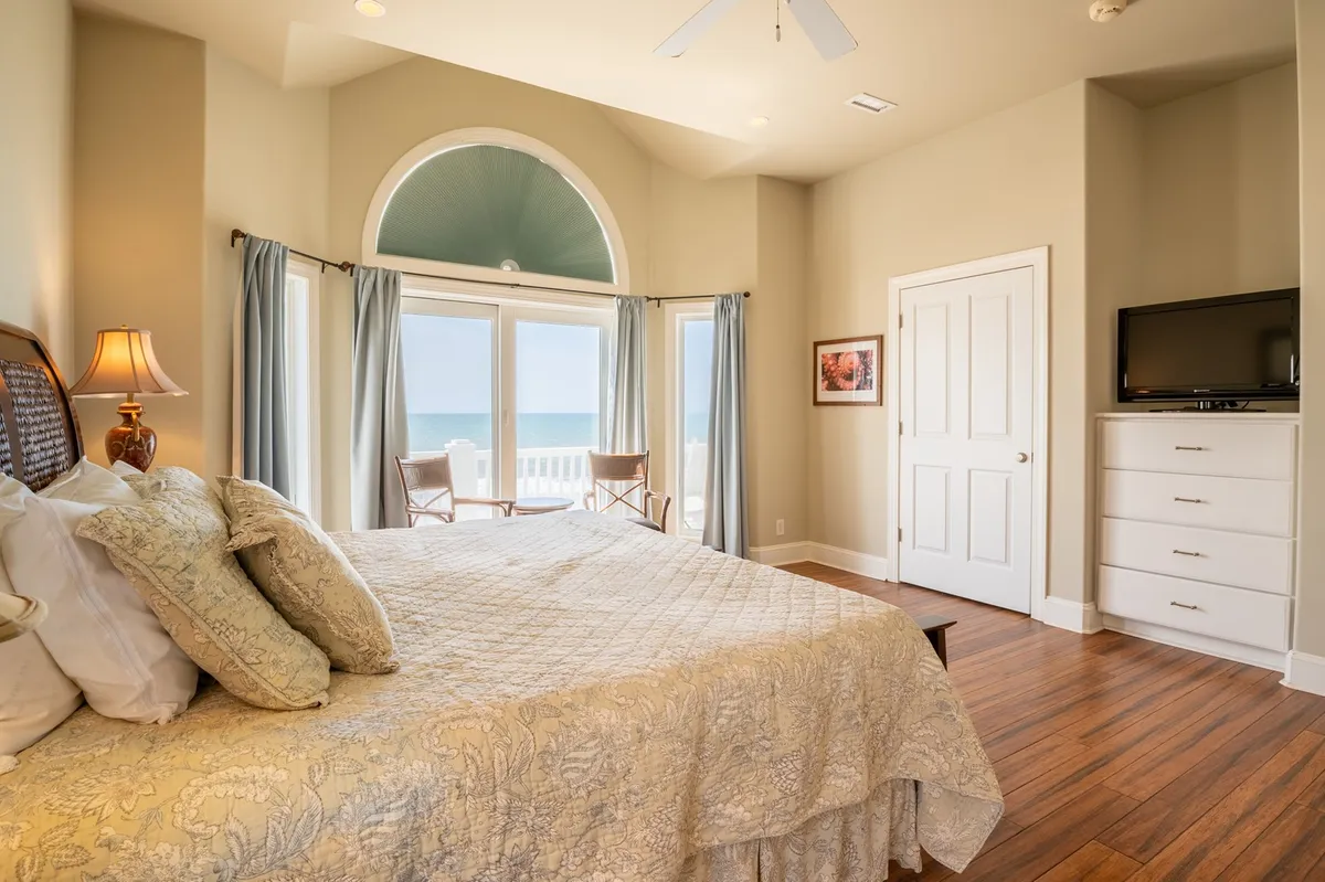A luxurious king suite featuring a large bed with decorative bedding positioned to face expansive windows, offering breathtaking ocean views. The suite includes a comfortable seating area on the balcony, perfect for enjoying the sunrise or sunset, and floods the space with natural light, creating an inviting sanctuary.
